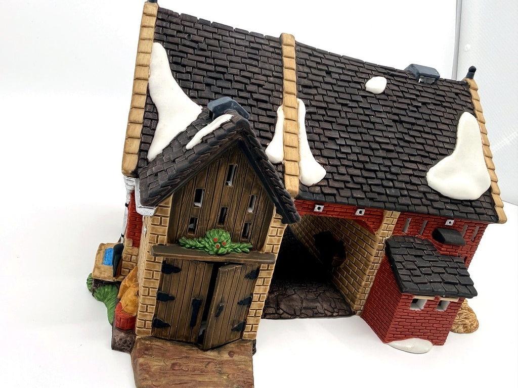 Department 56 Dickens' Village Butter Tub Barn #58338 – front three-quarter view: stone tower with wooden double doors and holly swag, covered archway, red brick, snow-dusted shingle roofs