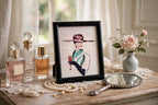 Styled lifestyle photo — the small Art Deco lady framed artwork (9.5 × 11.5 in) on a dressing-table vanity with perfume bottles and pearls (display inspiration)