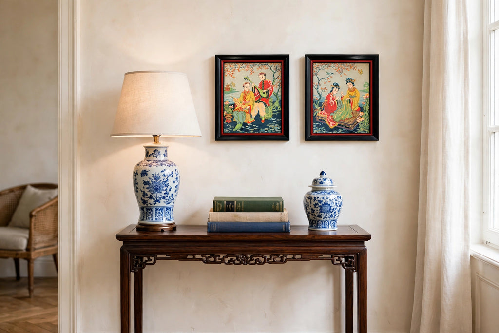 Styled lifestyle photo — the small framed Asian textile pair (17 × 14 in each) above a dark-wood side table with a porcelain lamp (display inspiration)