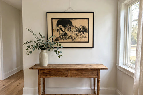 Styled lifestyle photo — the framed Bathers etching above a wooden console table in a bright entryway (display inspiration)
