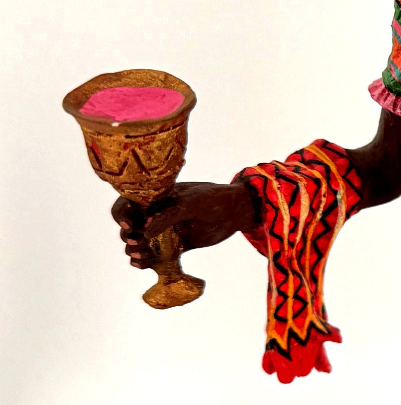 Detail crop — the gold unity cup and patterned ceremonial cloth in her hand
