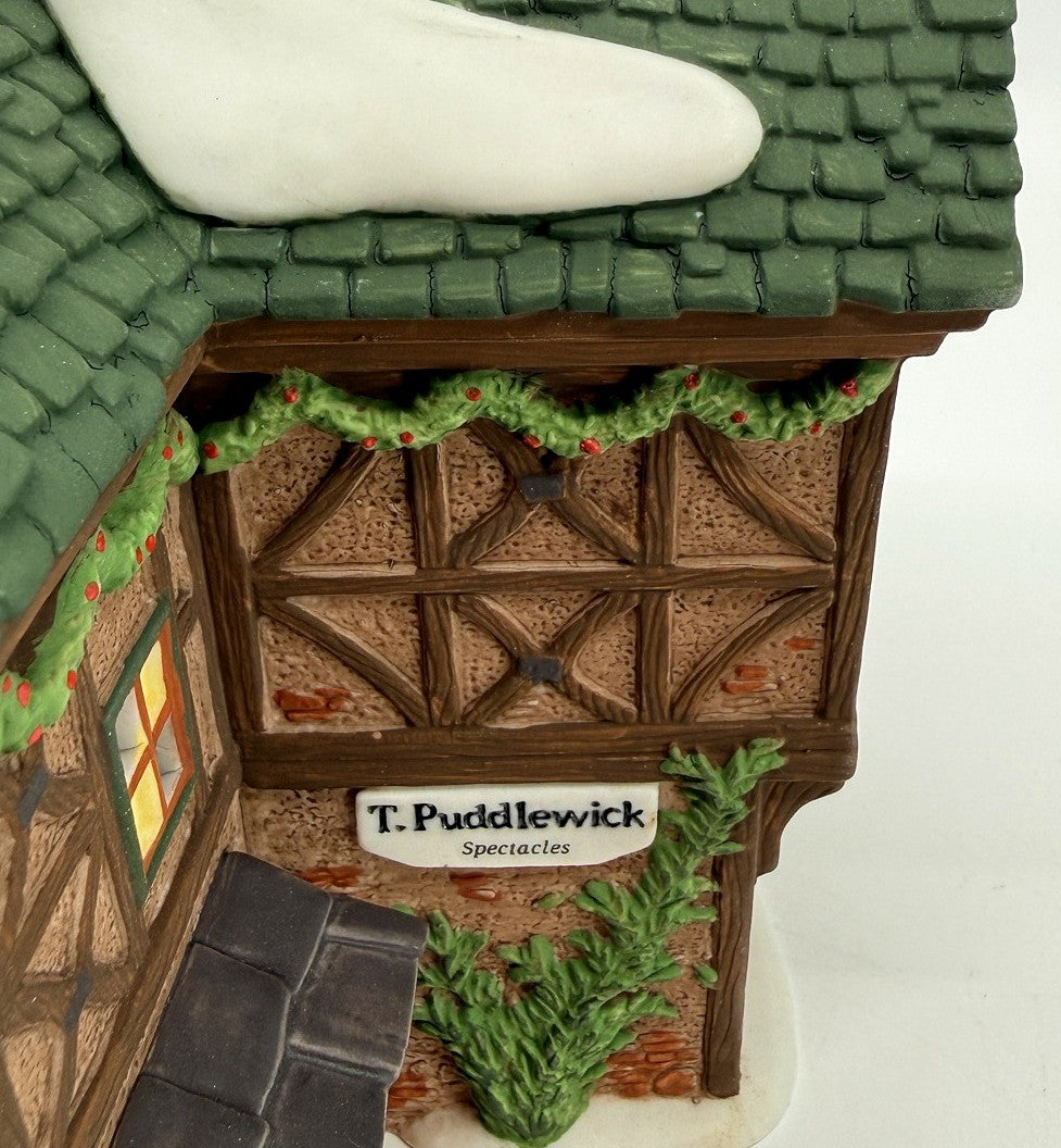 Department 56 Dickens' Village T. Puddlewick Spectacle Shop #58334 — detail: T. Puddlewick shop sign, garland, and half-timbered wall