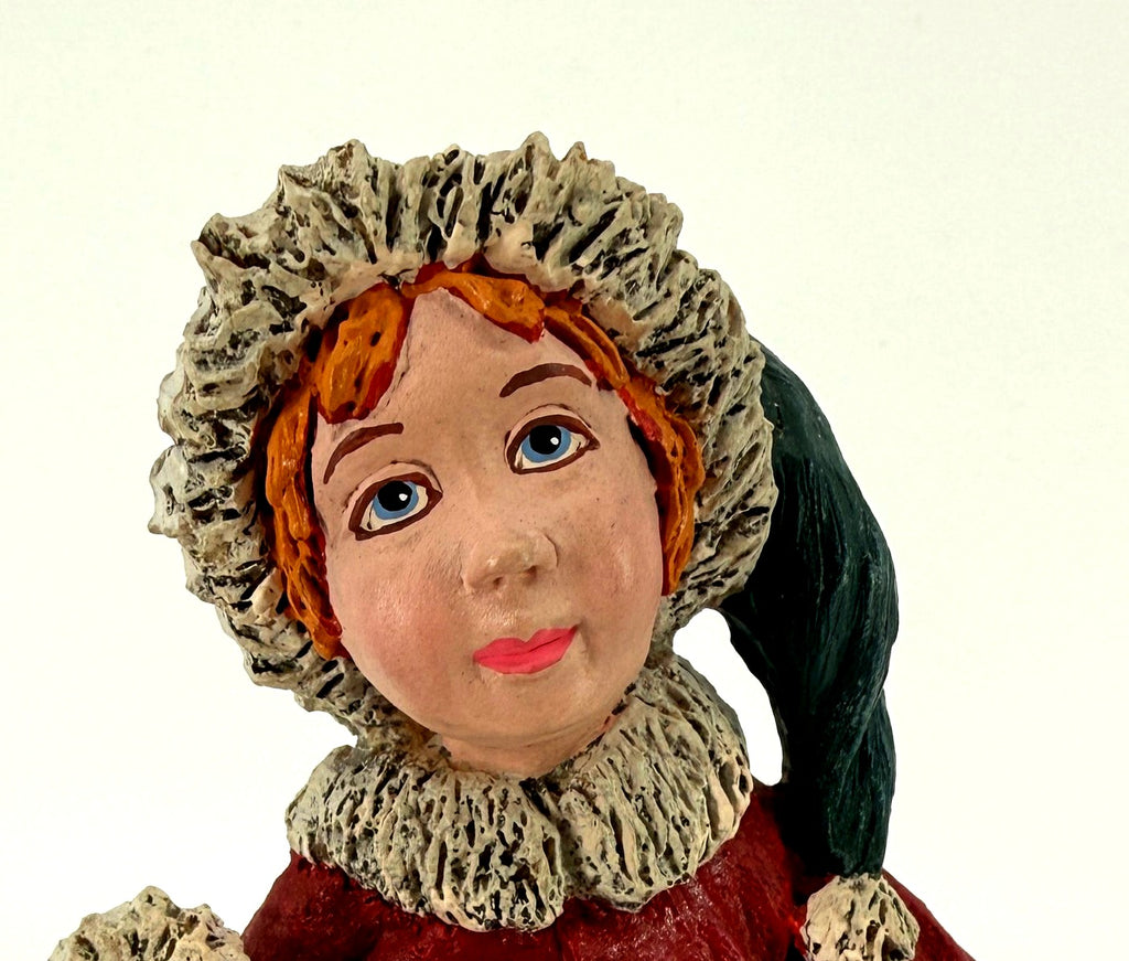 Close-up detail of the helper's hand-painted face — blue eyes, red hair, and the fur-trimmed green cap and collar