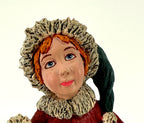 Close-up detail of the helper's hand-painted face — blue eyes, red hair, and the fur-trimmed green cap and collar