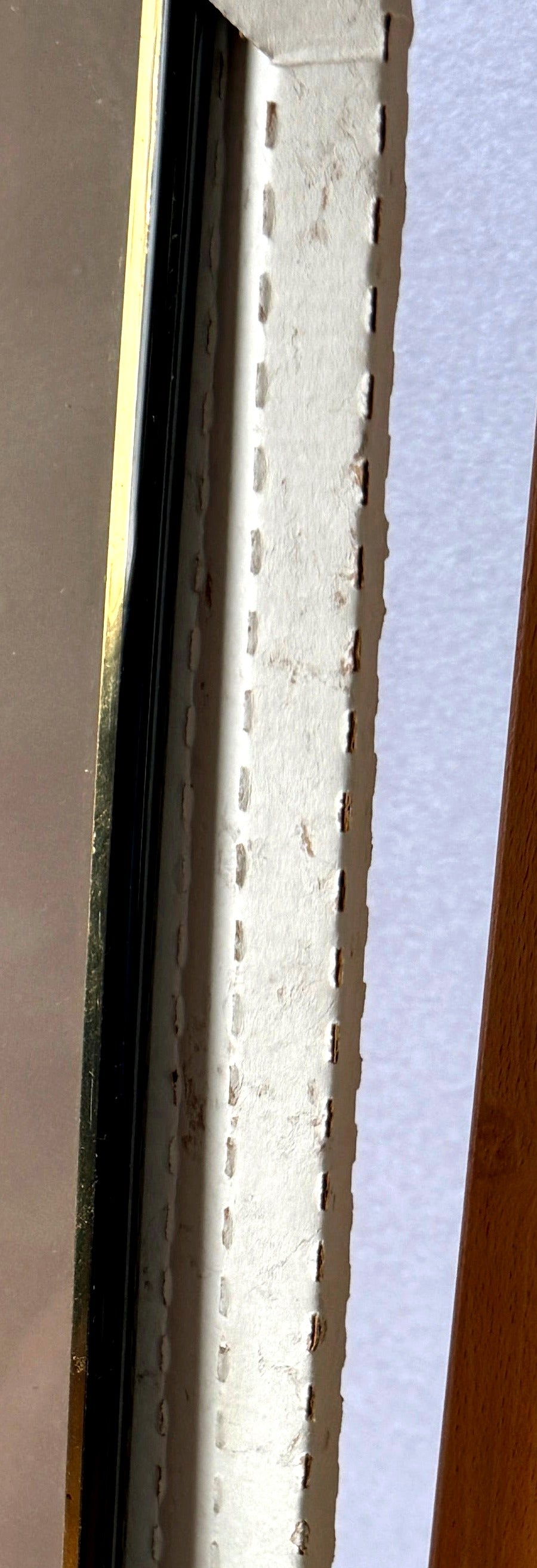 Detail crop — the frame's edge profile: black rail with gold-tone trim, with the original cardboard protector in place
