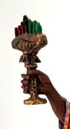 Detail crop — the kinara’s seven candles in red, black and green in his raised hand
