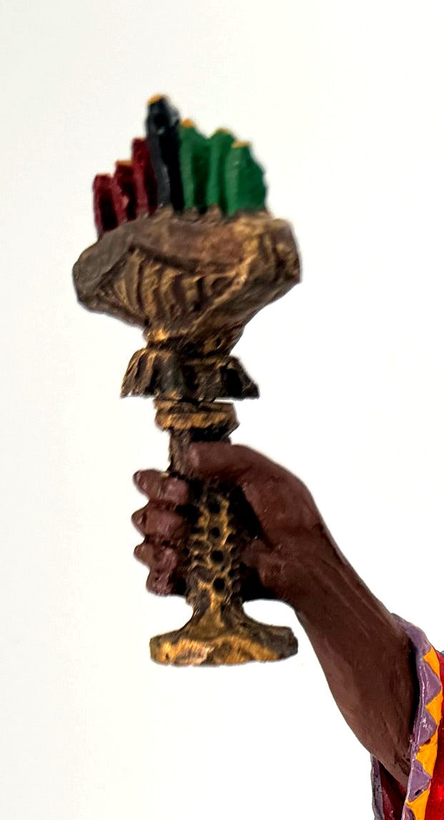 Detail crop — the kinara’s seven candles in red, black and green in his raised hand
