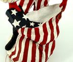 Detail close-up — the star-spangled gift going into the oversized red-and-white striped toy sack, tall black boot beside it