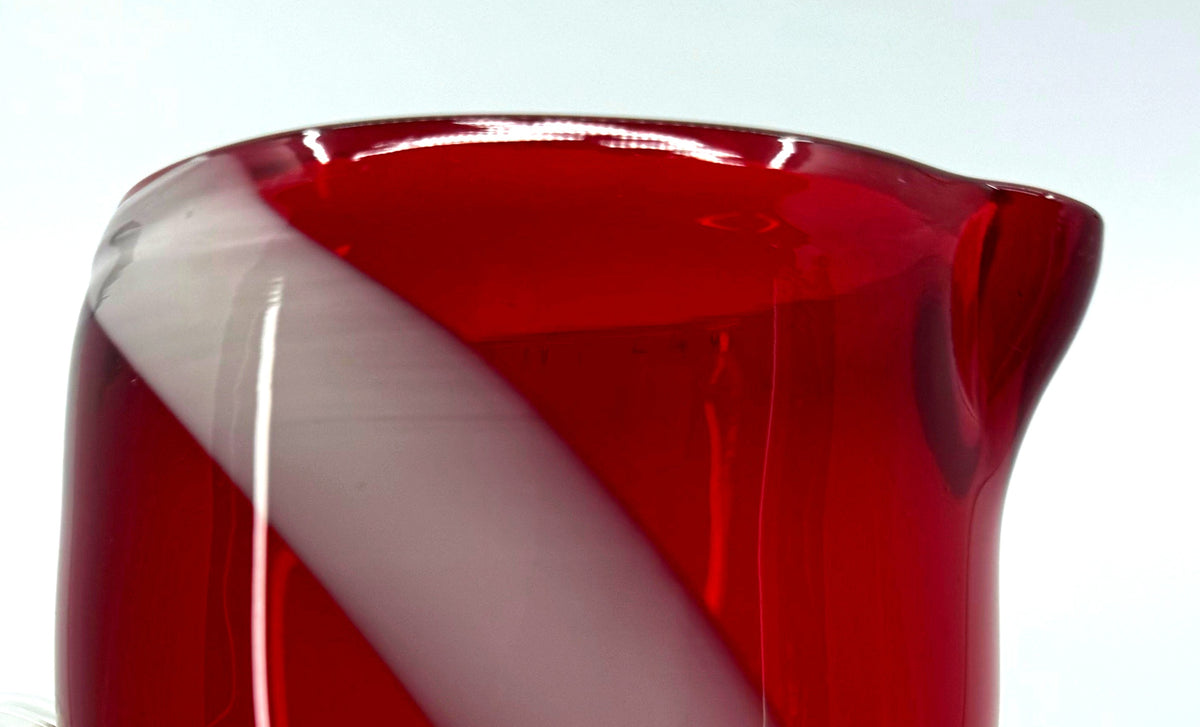 Close-up detail — the pinched pouring spout and rim of the pitcher, with the white swirl reaching the top of the glass