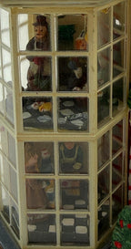 Close-up of the left bay tower interior scenes — a shopkeeper in a top hat above and children at the candy counter below, seen through the glass panes