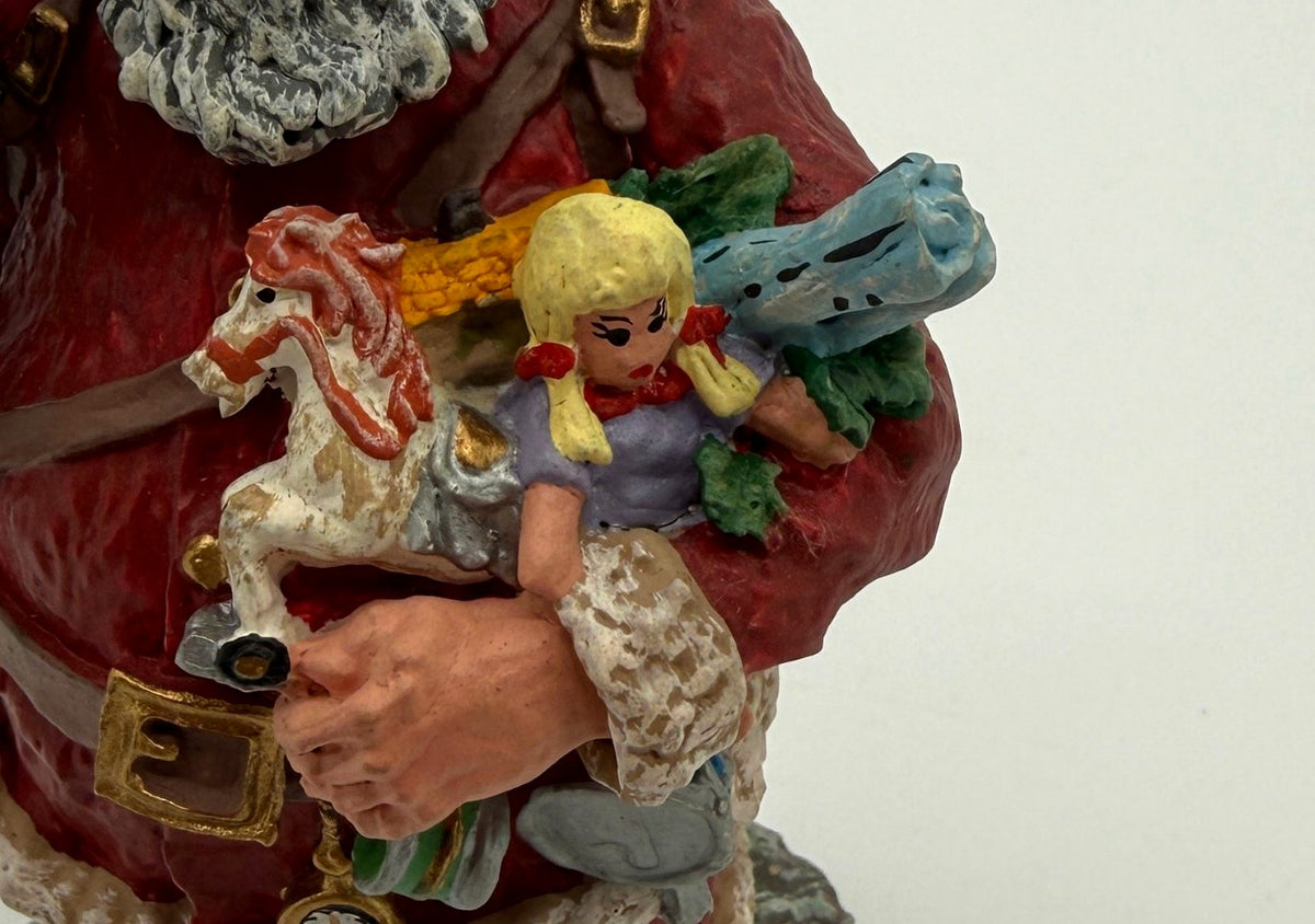 Vintage 1991 Duncan Royale Today's Nast Santa figurine – detail of the toys in Santa's arm: rocking horse, blonde doll, blue toy train and an ear of corn