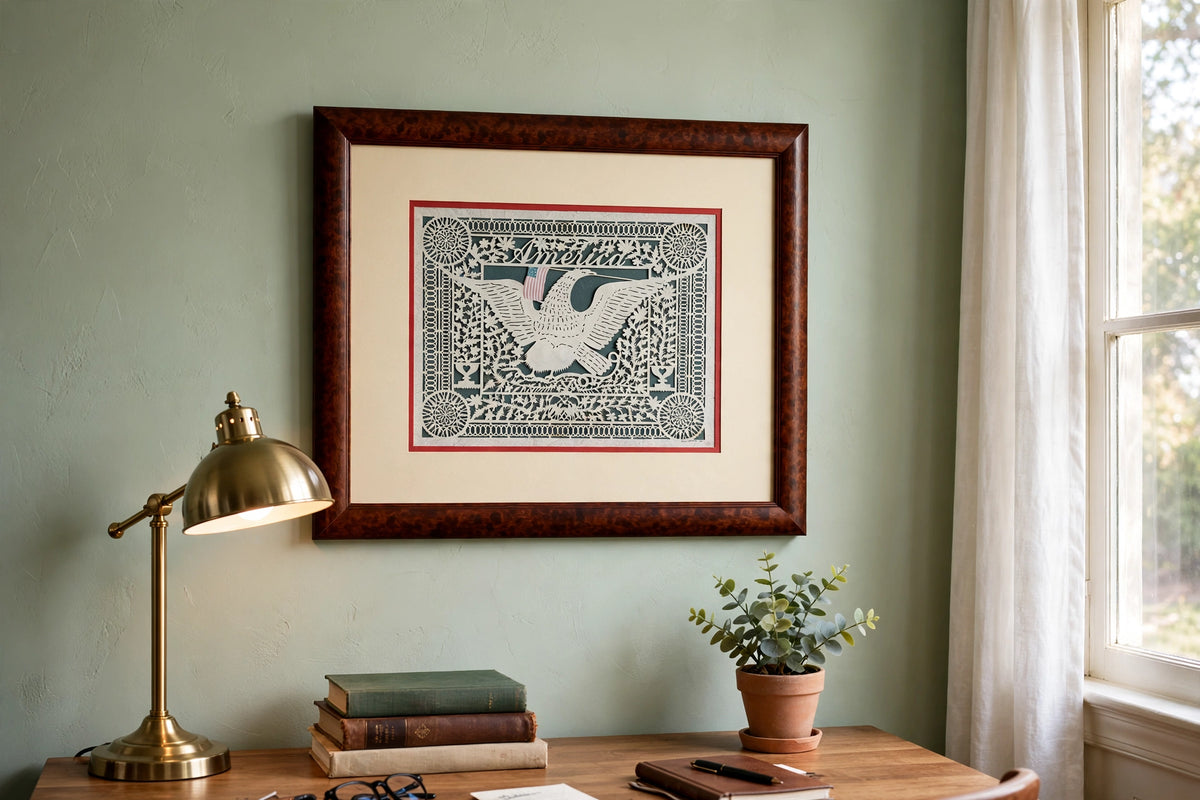 Styled lifestyle photo — the framed Eavenson ‘America’ scherenschnitte (23 × 19 in) above a desk in a home office (display inspiration)