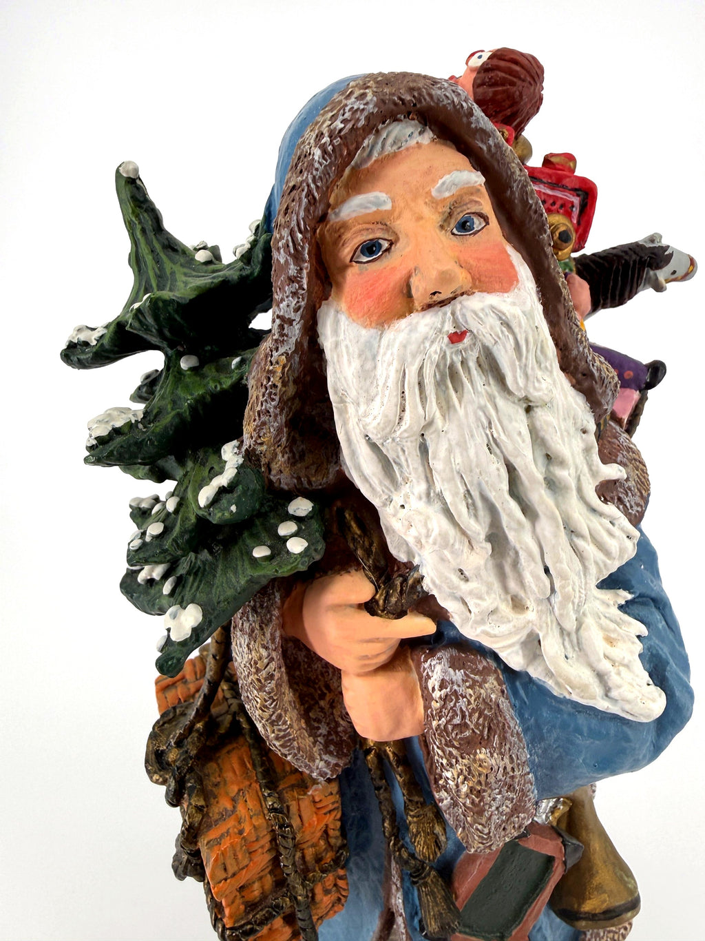 Close-up of Winter Santa’s face — hand-painted blue eyes, rosy cheeks and flowing white beard, snow-dusted evergreen beside him