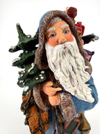 Close-up of Winter Santa’s face — hand-painted blue eyes, rosy cheeks and flowing white beard, snow-dusted evergreen beside him