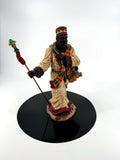 African American Santa figurine front view on a black display disc — cream robe, African-pattern scarf, jeweled crown, staff with red tassel, and gift sack