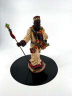 African American Santa figurine front view on a black display disc — cream robe, African-pattern scarf, jeweled crown, staff with red tassel, and gift sack