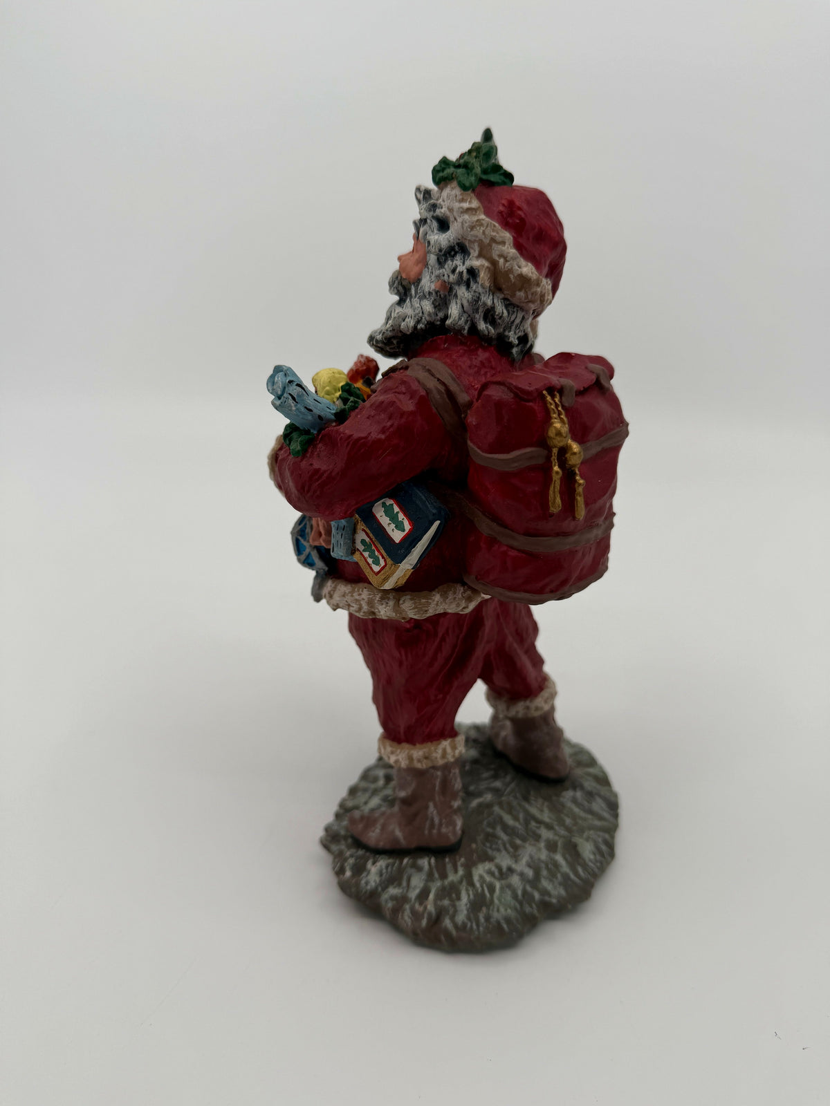 Vintage 1991 Duncan Royale Today's Nast Santa figurine – back three-quarter view: red toy sack worn backpack-style with gold bell tassels and a book tucked under his arm