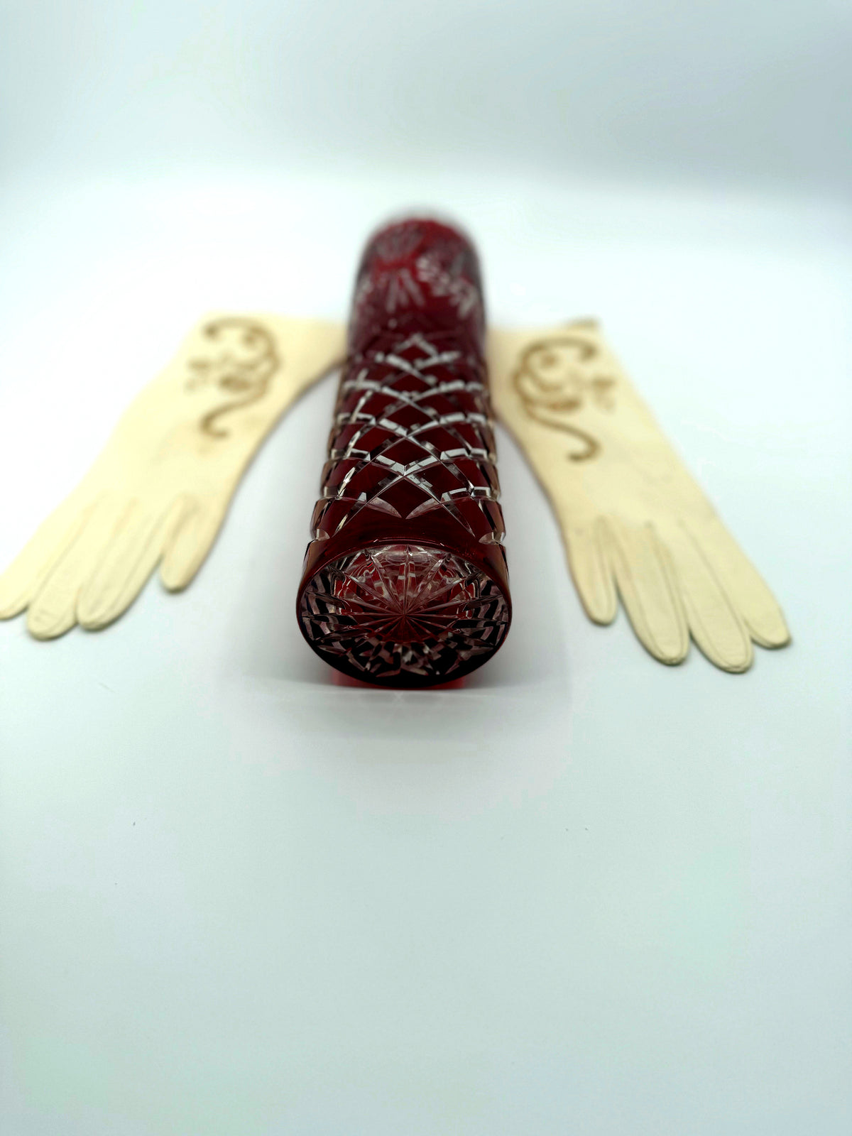 Vintage ruby red cut-to-clear glass vase, 12 inch — the vase lying on its side showing the star-cut base, gloves behind
