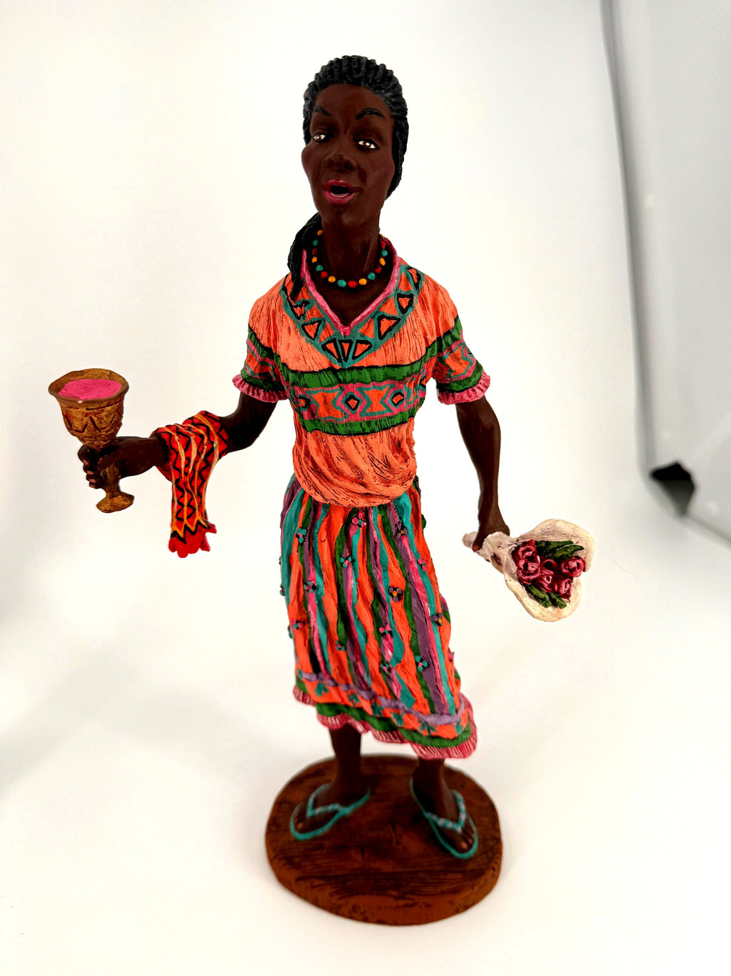 The female Kwanzaa figure alone — coral dress, unity cup and cloth in one hand, bouquet of roses in the other