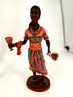 The female Kwanzaa figure alone — coral dress, unity cup and cloth in one hand, bouquet of roses in the other