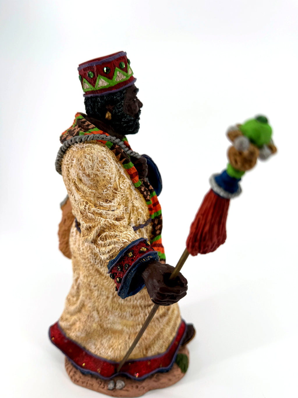 Side view close — jeweled crown, patterned scarf, decorated cuff and staff