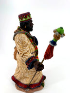 Side view close — jeweled crown, patterned scarf, decorated cuff and staff