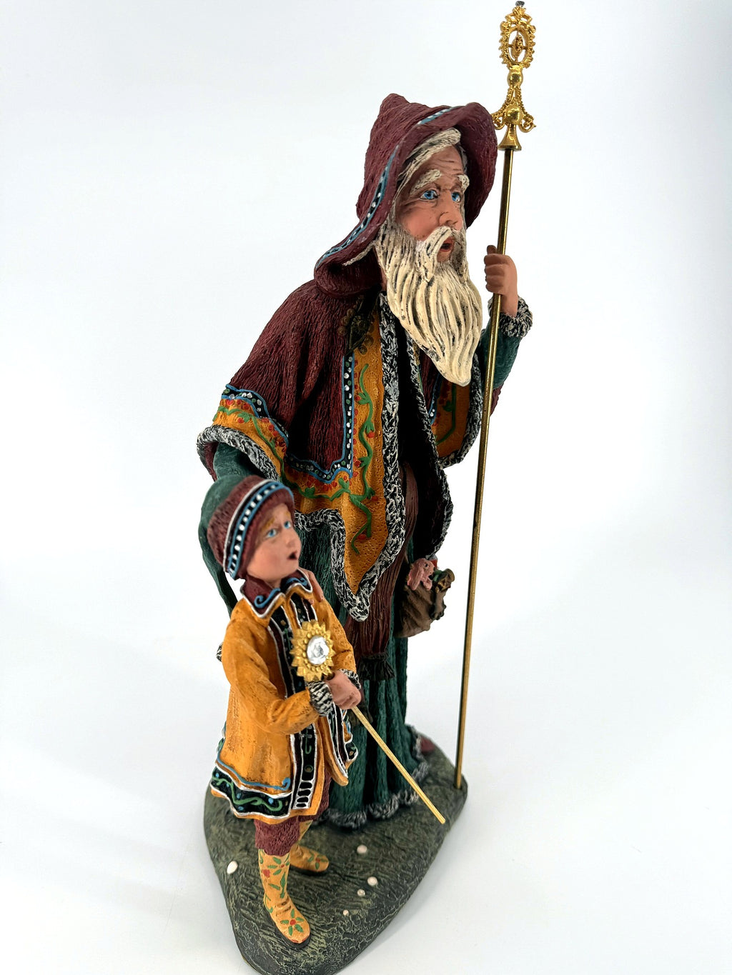 Front view from the left — the child's sun-medallion staff, golden ochre coat and decorated boots