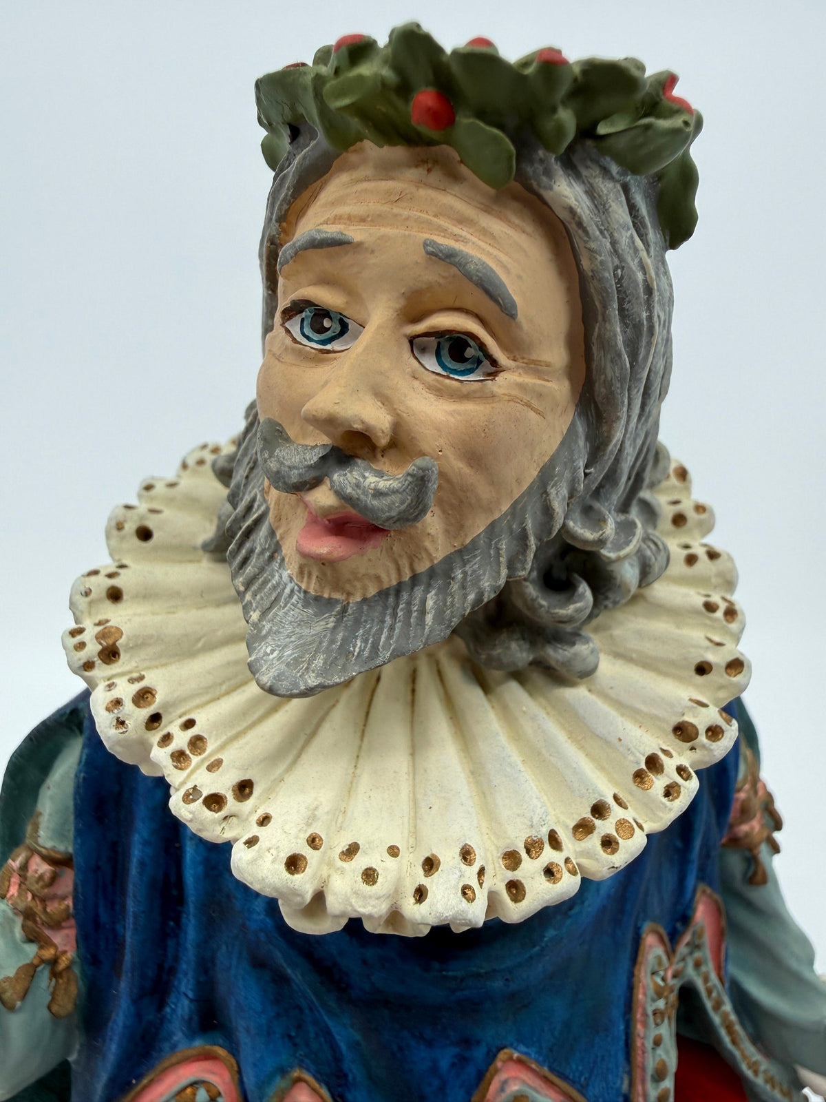 Vintage 1985 Duncan Royale Sir Christmas figurine – close-up of the face: blue eyes, curled silver mustache and beard, holly wreath with red berries, lace ruff with gold eyelet dots