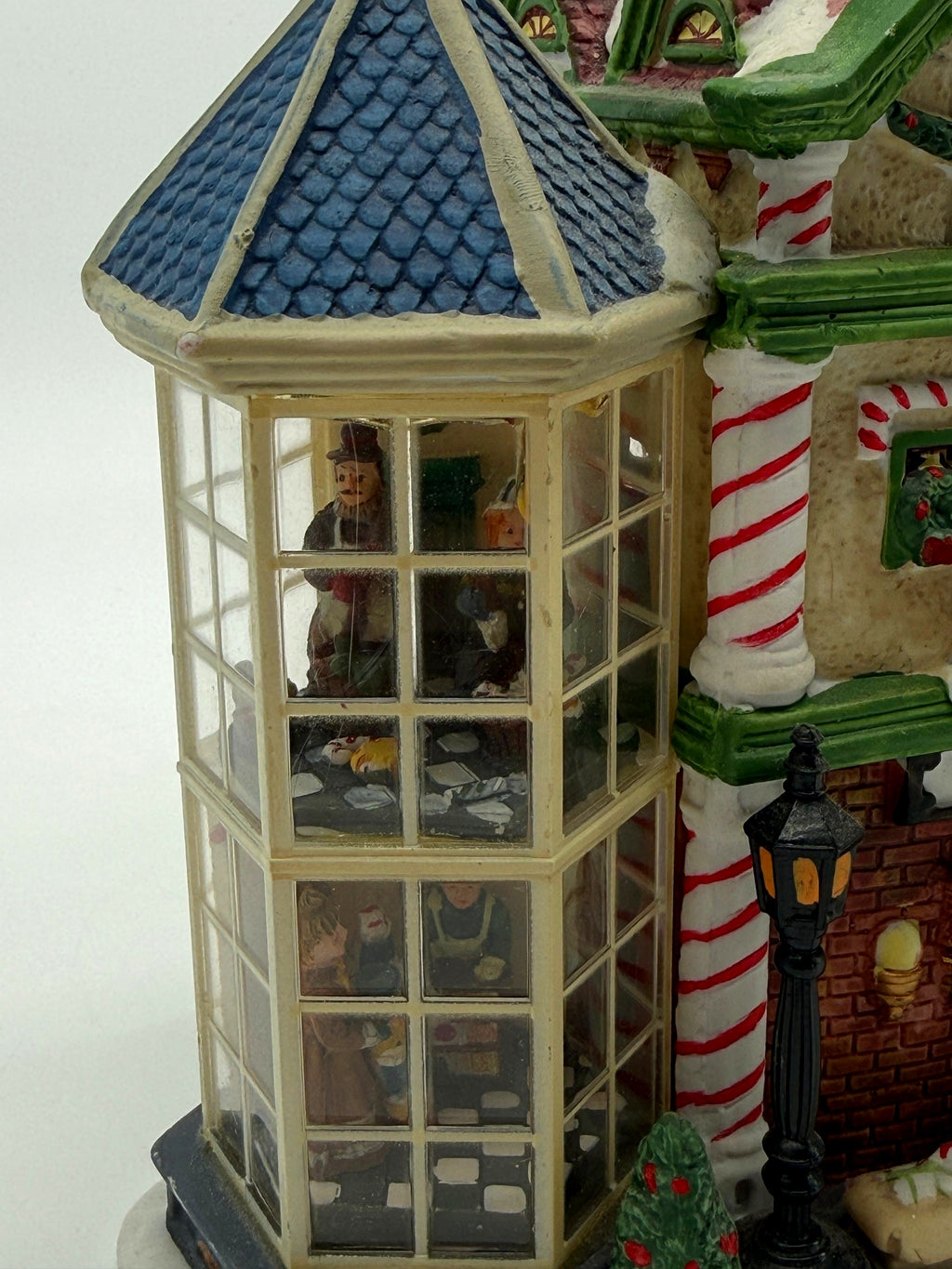 Close-up of the left glass bay tower with its blue shingled roof and two floors of interior figure scenes