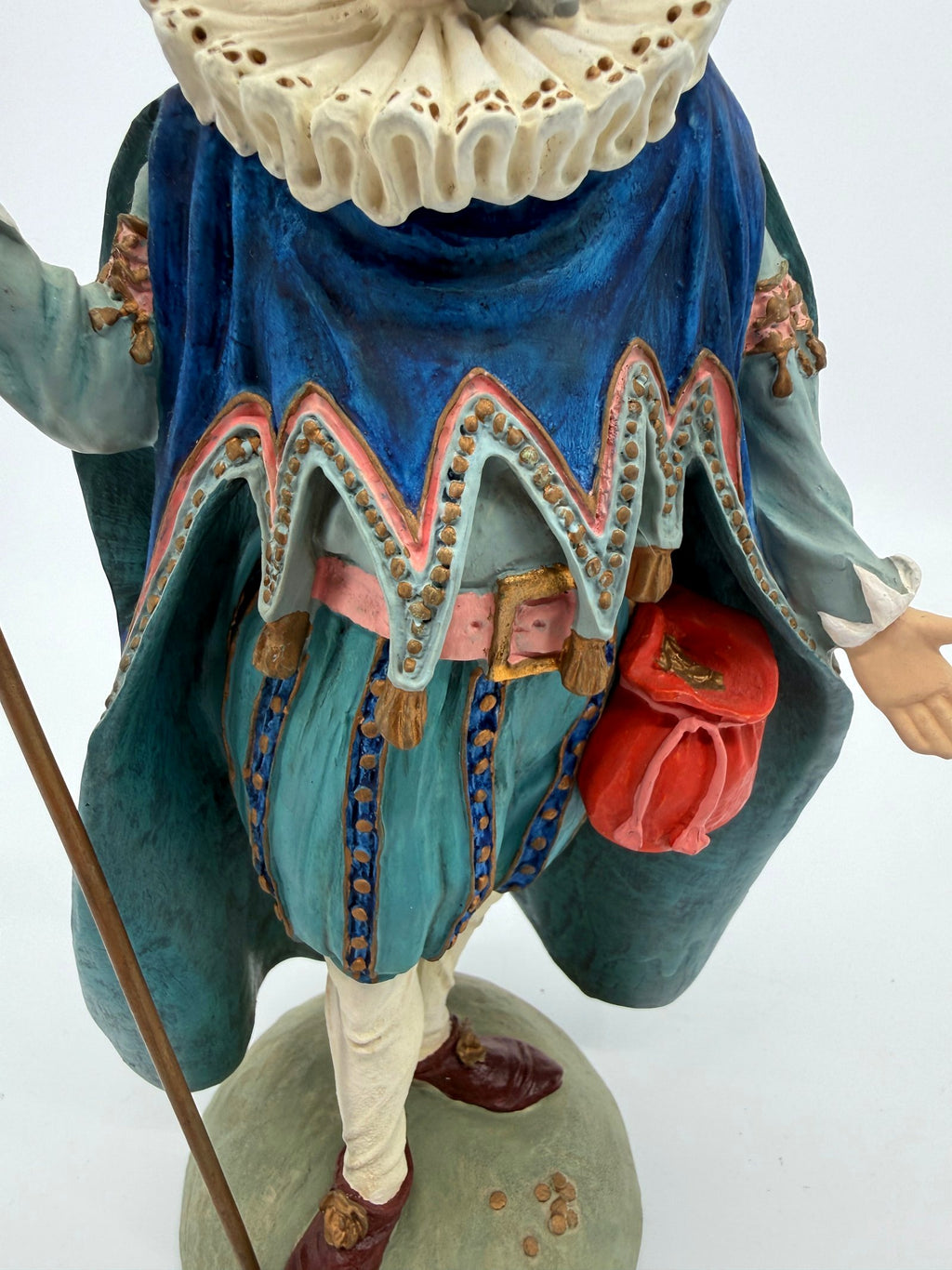 Vintage 1985 Duncan Royale Sir Christmas figurine – close-up of the costume: scalloped gold-dotted cape trim, pink sash with gold buckle and tassels, red drawstring pouch, teal trunk hose