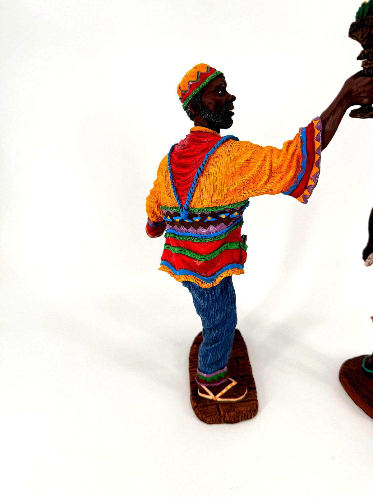 The male figure from behind at three-quarters — the red drape and patterned bands of his tunic