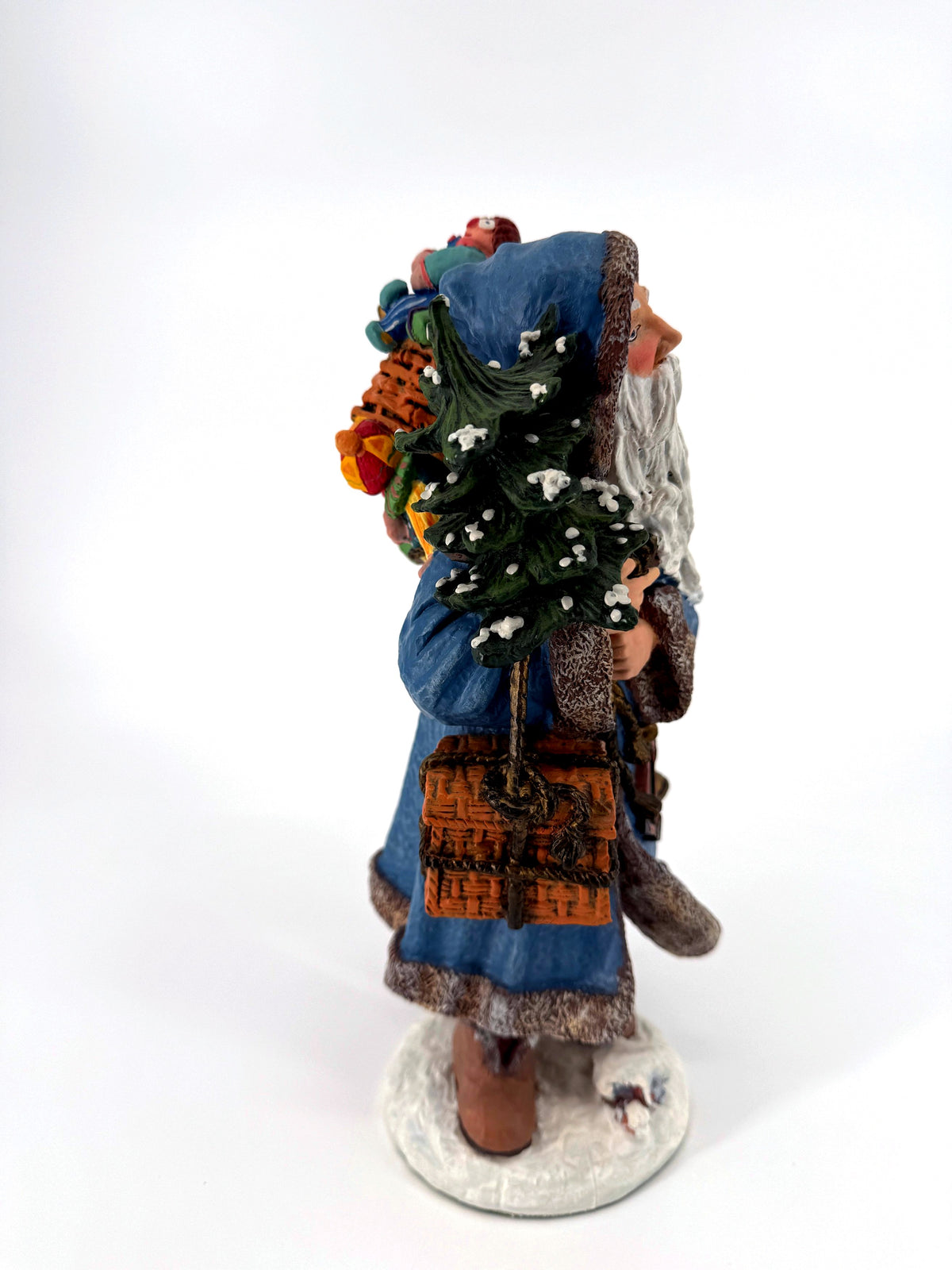 Side profile of Winter Santa carrying the snow-dusted Christmas tree, toy pack on his back