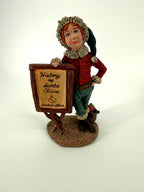 Duncan Royale History of Santa Claus Signature Piece - front view of the helper figure with his hand on the sign, fur-trimmed green cap and textured base