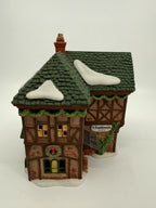 Department 56 Dickens' Village T. Puddlewick Spectacle Shop #58334 — front view: half-timbered facade, green shingled roof with snow, wreath, T. Puddlewick sign