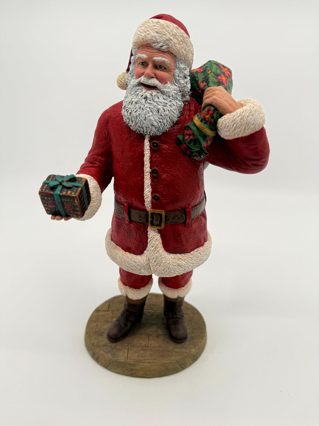 Vintage 1994 Duncan Royale Santa's Gift figurine – front view; Santa in a deep red suit with white fur trim, green poinsettia gift sack over his shoulder and a wrapped present in hand