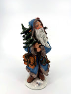 Winter Santa front view from his left — fur-trimmed hood, flowing white beard and snow-dusted tree