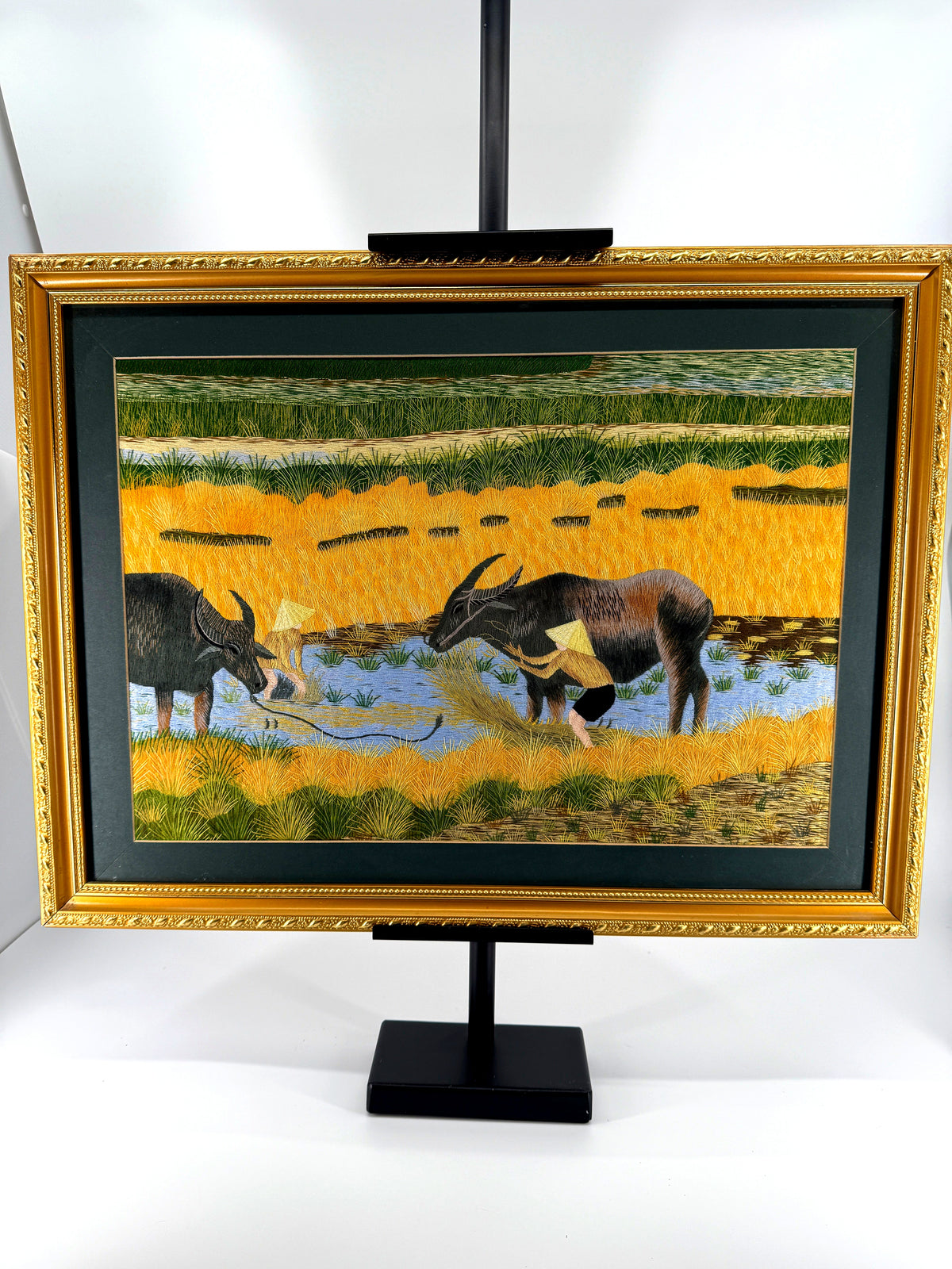 Signed Vietnamese hand-embroidered textile art — water buffalo in rice terraces — the framed piece on its stand, front view