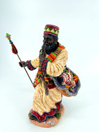 Front three-quarter view with the staff, kente-style woven scarf and shoulder sack of gifts