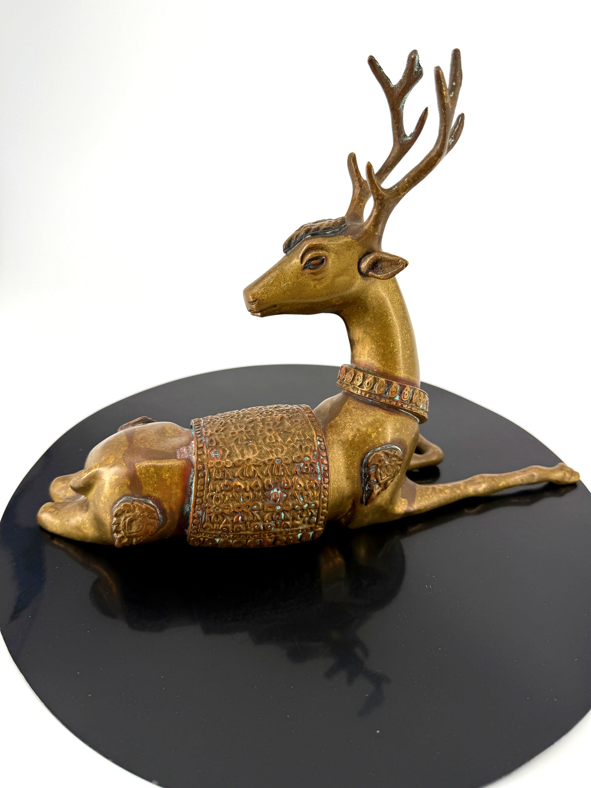 Vintage brass reclining stag figurine with ornate saddle — side profile on the black base