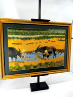 Signed Vietnamese hand-embroidered textile art — water buffalo in rice terraces — the framed piece on its stand, angled from the right