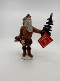 Vintage 1983 Duncan Royale Pioneer Santa figurine – front view with the original red collector's booklet hanging from the tree; brown fur-trimmed pioneer outfit and flag-decorated Christmas tree