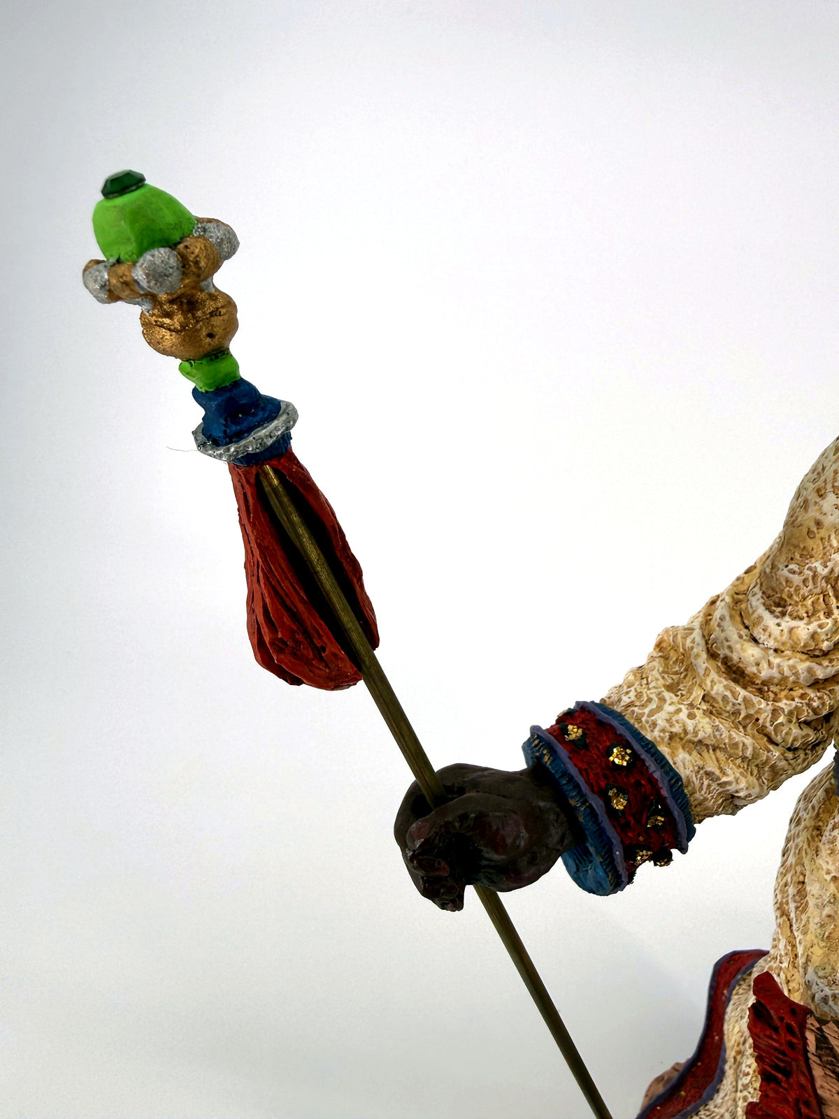 Close-up of the staff top — green finial, gold and silver beads and red tassel
