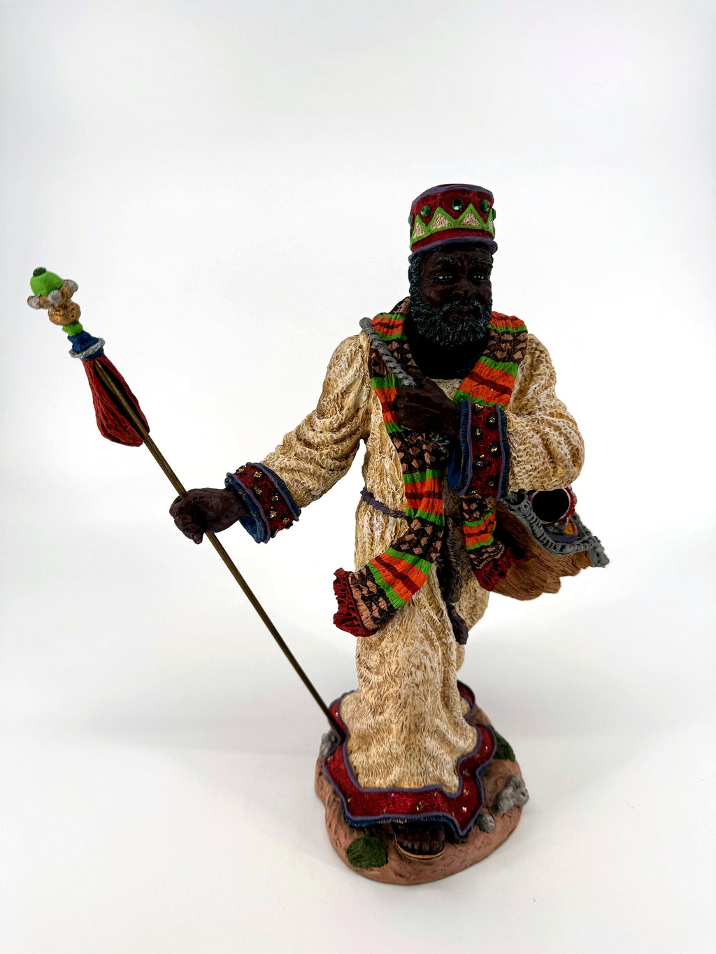 Front view — cream robe with red hem trim, woven scarf, jeweled crown, staff and rocky base