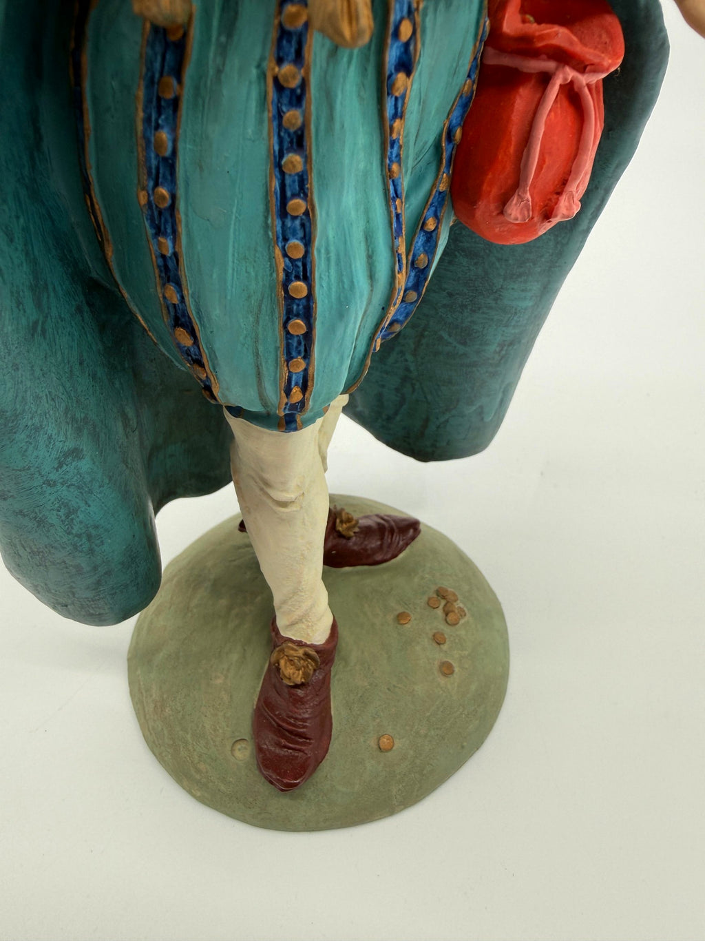 Vintage 1985 Duncan Royale Sir Christmas figurine – close-up of the legs and round sage-green base: teal trunk hose with blue-and-gold dotted bands, burgundy shoes, tiny gold coins scattered at his feet
