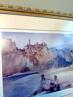 Detail view — the upper artwork and ornate gold frame top rail: the cliff-top village and church spire