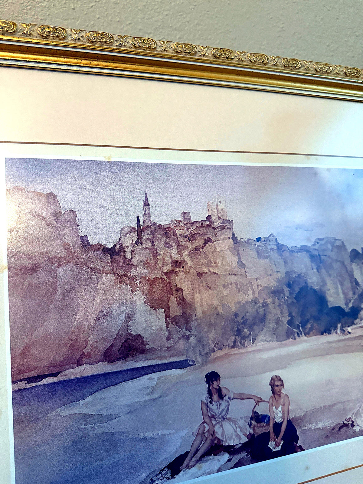 Detail view — the upper artwork and ornate gold frame top rail: the cliff-top village and church spire