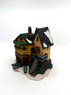 Department 56 Dickens' Village "The Grapes Inn" lighted porcelain building – three-quarter view showing the stone staircase, balcony and snow-dusted roofs