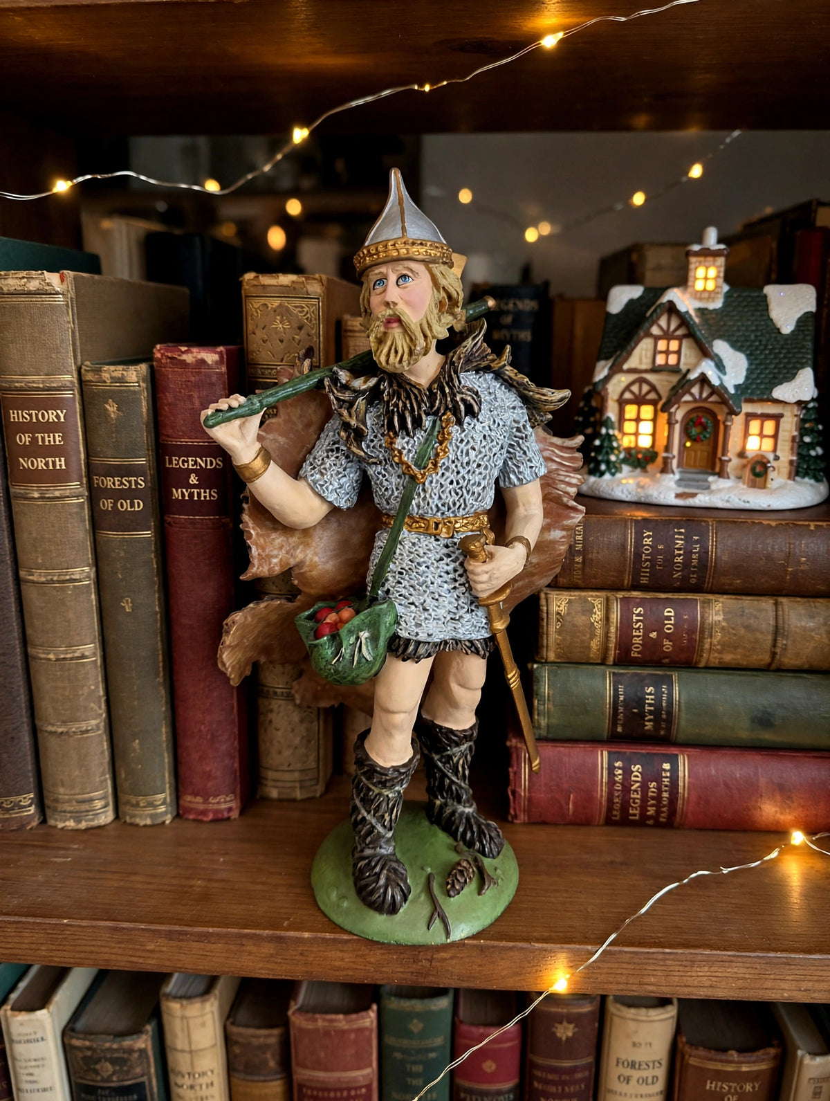 Odin on a bookshelf with a lit Christmas village house (styled display inspiration)