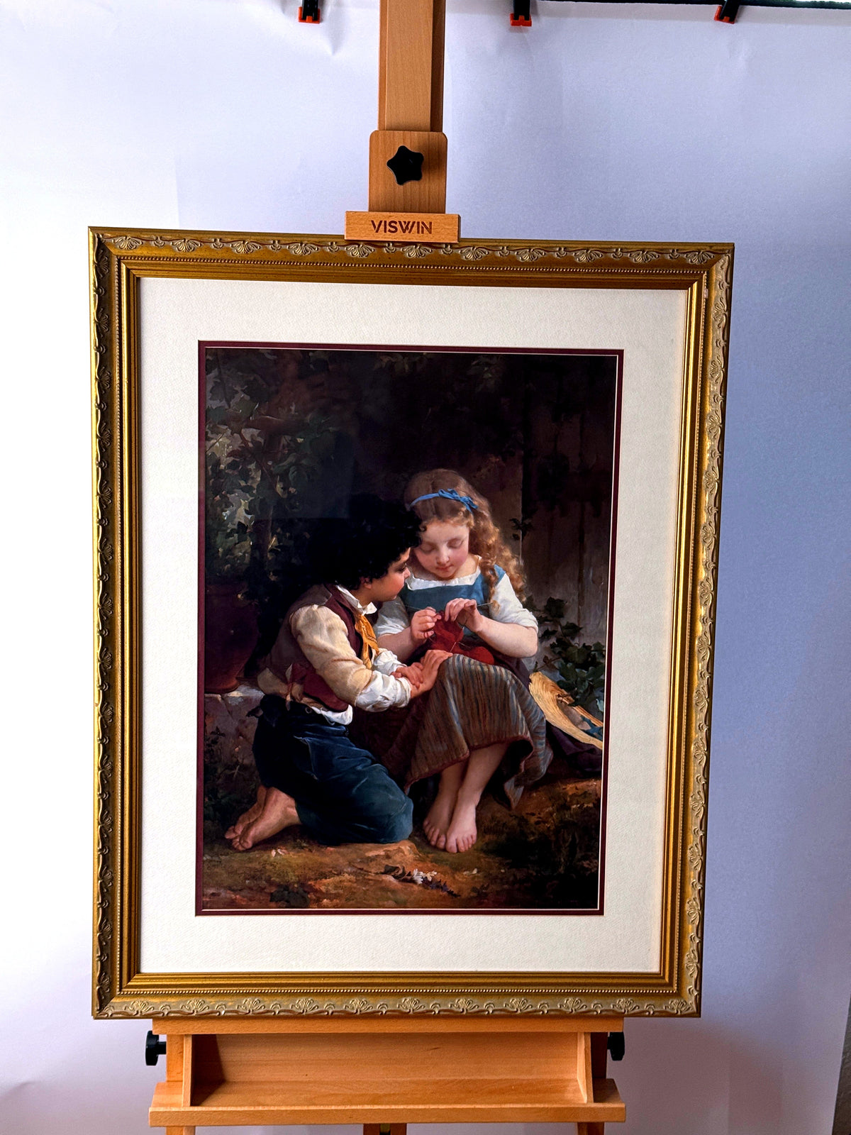 Emile Munier The Knitting Lesson framed art print — front view on an easel, wider shot