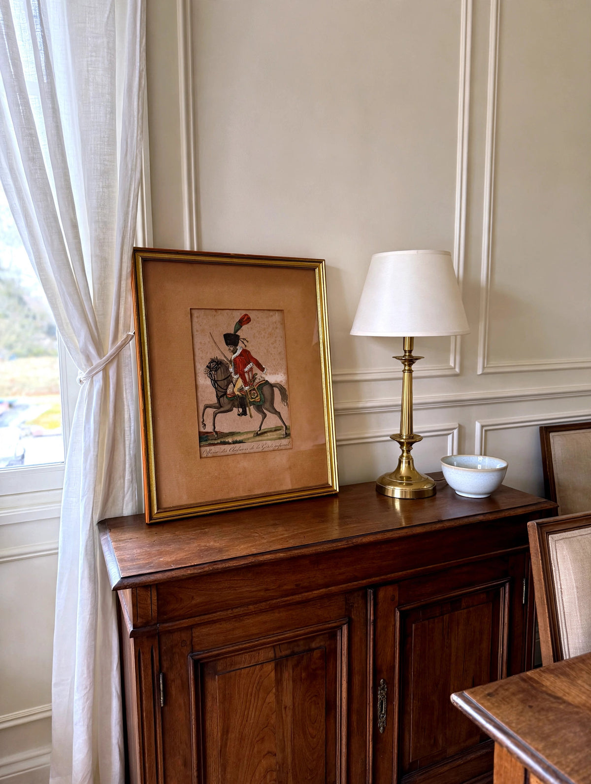 Styled lifestyle photo — the framed Martinet chasseur engraving leaning on a dark wood sideboard in a bright dining room (display inspiration)